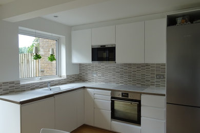Design ideas for a scandinavian l-shaped eat-in kitchen in Cambridgeshire with a single-bowl sink, white cabinets, laminate benchtops, grey splashback, ceramic splashback, stainless steel appliances, light hardwood floors and no island.