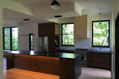 Inspiration for a mid-sized modern u-shaped light wood floor and gray floor eat-in kitchen remodel in New York with an undermount sink, flat-panel cabinets, medium tone wood cabinets, soapstone countertops, white backsplash, stainless steel appliances, an island and black countertops