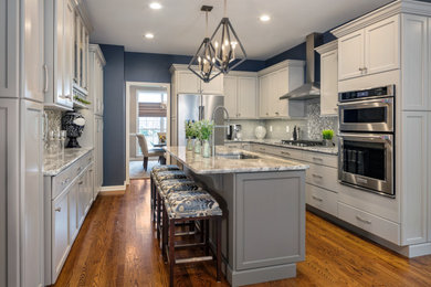 Example of a mid-sized transitional l-shaped medium tone wood floor, brown floor and tray ceiling eat-in kitchen design in Other with glass tile backsplash, stainless steel appliances, an undermount sink, shaker cabinets, gray cabinets, granite countertops, an island, multicolored backsplash and gray countertops