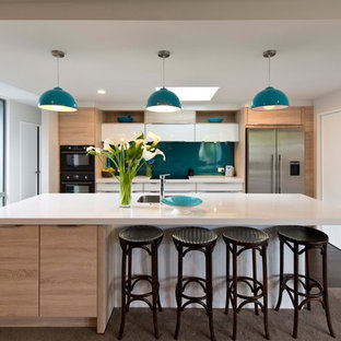 Идея дизайна: параллельная кухня среднего размера в современном стиле с кладовкой, врезной раковиной, белыми фасадами, столешницей из кварцевого композита, черной техникой, полом из ламината, островом и коричневым полом