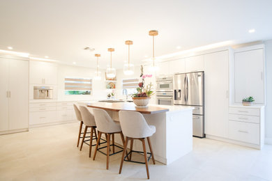 Inspiration for a large modern l-shaped porcelain tile and beige floor eat-in kitchen remodel in Miami with a farmhouse sink, flat-panel cabinets, beige cabinets, quartzite countertops, white backsplash, stone slab backsplash, stainless steel appliances, two islands and white countertops
