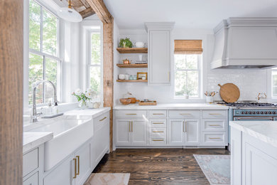 Large country l-shaped open plan kitchen in Boston with a farmhouse sink, white splashback, with island and white benchtop.