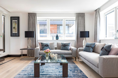 This is an example of a large contemporary formal open plan living room in London with white walls, light hardwood flooring, no fireplace, no tv and beige floors.