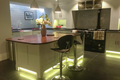 Inspiration for a large bohemian l-shaped open plan kitchen in London with shaker cabinets, beige cabinets, wood worktops, black splashback, a breakfast bar and brown worktops.