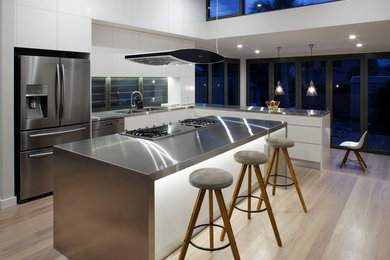 Design ideas for a large contemporary l-shaped open plan kitchen in Sydney with an undermount sink, flat-panel cabinets, white cabinets, stainless steel benchtops, white splashback, mosaic tile splashback, stainless steel appliances, light hardwood floors and with island.