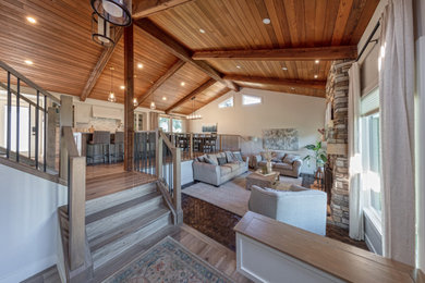 Example of a mid-sized country loft-style medium tone wood floor, brown floor and exposed beam living room design in Edmonton with white walls, a standard fireplace and a stacked stone fireplace