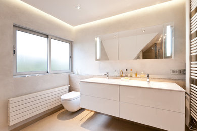 Inspiration for a large modern master bathroom in Strasbourg with an undermount tub, a curbless shower, a wall-mount toilet, beige tile, grey walls, a console sink, solid surface benchtops, flat-panel cabinets, white cabinets, ceramic floors, beige floor and white benchtops.