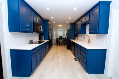 Mid-sized trendy galley laminate floor and beige floor eat-in kitchen photo in Other with shaker cabinets, blue cabinets, quartz countertops, white backsplash, subway tile backsplash, no island, white countertops, an undermount sink and black appliances