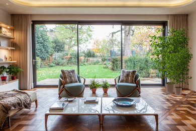 This is an example of a large contemporary formal and grey and brown open plan living room feature wall in London with white walls, light hardwood flooring, a two-sided fireplace, a plastered fireplace surround, brown floors and a coffered ceiling.