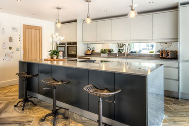 Design ideas for a mid-sized contemporary galley eat-in kitchen in Cheshire with a drop-in sink, flat-panel cabinets, grey cabinets, granite benchtops, mirror splashback, panelled appliances, medium hardwood floors, a peninsula and brown floor.