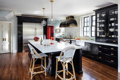 Design ideas for a large country l-shaped eat-in kitchen in New York with recessed-panel cabinets, black cabinets, grey splashback, stainless steel appliances, dark hardwood floors, with island, brown floor, a farmhouse sink, quartz benchtops, stone slab splashback and white benchtop.