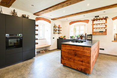 Moderne Küche mit integriertem Waschbecken, Granit-Arbeitsplatte, Küchenrückwand in Weiß, Kalk-Rückwand, Küchengeräten aus Edelstahl, Betonboden, grauem Boden, grauer Arbeitsplatte und freigelegten Dachbalken in Nürnberg