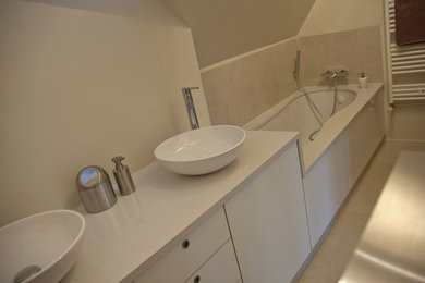 パリにある中くらいなコンテンポラリースタイルのおしゃれなマスターバスルーム (インセット扉のキャビネット、白いキャビネット、アンダーマウント型浴槽、アルコーブ型シャワー、壁掛け式トイレ、ベージュのタイル、セラミックタイル、ベージュの壁、セラミックタイルの床、ベッセル式洗面器、珪岩の洗面台、ベージュの床) の写真