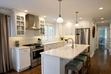 Inspiration for a large transitional u-shaped eat-in kitchen in Bridgeport with a farmhouse sink, recessed-panel cabinets, white cabinets, quartz benchtops, white splashback, subway tile splashback, stainless steel appliances, dark hardwood floors, with island, brown floor and white benchtop.