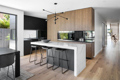 This is an example of a modern galley eat-in kitchen in Melbourne with raised-panel cabinets, medium wood cabinets, quartz benchtops, glass sheet splashback, stainless steel appliances and multiple islands.