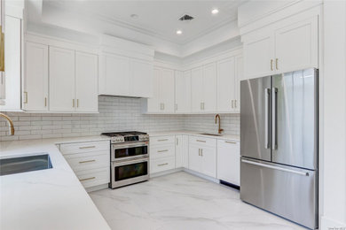 Example of a mid-sized classic u-shaped marble floor and white floor open concept kitchen design in New York with an undermount sink, shaker cabinets, white cabinets, quartz countertops, white backsplash, subway tile backsplash, stainless steel appliances, no island and white countertops