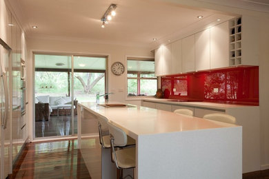 Design ideas for a large contemporary galley separate kitchen in Brisbane with flat-panel cabinets, white cabinets, solid surface benchtops, red splashback, glass sheet splashback, medium hardwood floors and with island.