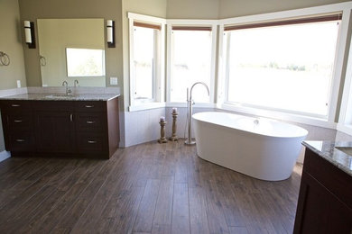 This is an example of a large modern master bathroom in Calgary with shaker cabinets, dark wood cabinets, a freestanding tub, multi-coloured tile, stone slab, terrazzo benchtops, a two-piece toilet, beige walls, medium hardwood floors, an undermount sink and brown floor.