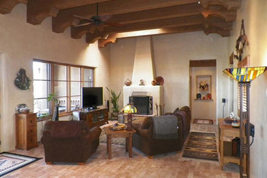Example of a large southwest enclosed brick floor, brown floor, exposed beam, vaulted ceiling and wood ceiling living room design in Albuquerque with white walls, a standard fireplace, a plaster fireplace and a tv stand