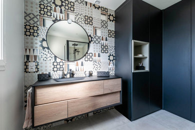 Inspiration for a mid-sized contemporary master bathroom in Lyon with black cabinets, a curbless shower, a wall-mount toilet, multi-coloured tile, ceramic tile, white walls, ceramic floors, a console sink, glass benchtops, beige floor, a hinged shower door, black benchtops, an enclosed toilet and a single vanity.