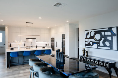 Example of a large minimalist l-shaped vinyl floor and beige floor eat-in kitchen design in San Diego with a drop-in sink, flat-panel cabinets, white cabinets, quartz countertops, white backsplash, quartz backsplash, black appliances, an island and white countertops