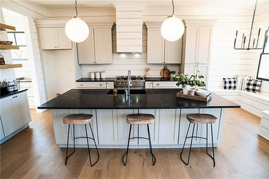 Inspiration for a mid-sized transitional l-shaped light wood floor and beige floor open concept kitchen remodel in Miami with an undermount sink, shaker cabinets, white cabinets, white backsplash, wood backsplash, stainless steel appliances, an island and black countertops