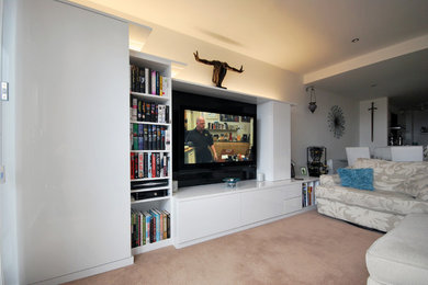 This is an example of a medium sized contemporary living room with white walls, carpet and a wall mounted tv.