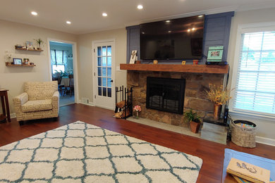 Example of a large transitional enclosed medium tone wood floor and brown floor living room design in Other with gray walls, a standard fireplace, a stone fireplace and a wall-mounted tv