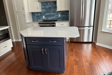 Mid-sized transitional u-shaped eat-in kitchen in Cincinnati with an undermount sink, recessed-panel cabinets, white cabinets, quartz benchtops, blue splashback, glass tile splashback, stainless steel appliances, medium hardwood floors, with island, brown floor and white benchtop.