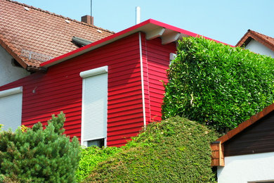 This is an example of a small contemporary one-storey red house exterior in Frankfurt with wood siding, a shed roof and a metal roof.