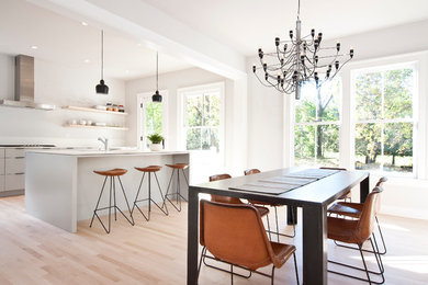 Example of a large minimalist l-shaped light wood floor and beige floor eat-in kitchen design in New York with an undermount sink, flat-panel cabinets, white cabinets, solid surface countertops, stainless steel appliances and an island