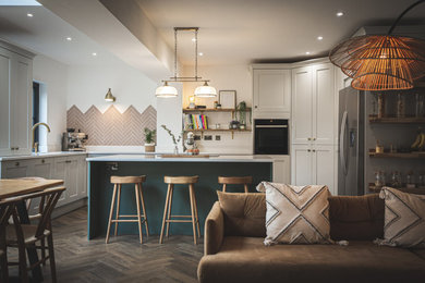 Medium sized traditional grey and teal l-shaped open plan kitchen in Devon with an integrated sink, shaker cabinets, green cabinets, black appliances, an island, brown floors, white worktops and feature lighting.
