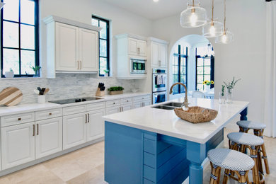 Inspiration for a large coastal galley travertine floor and beige floor kitchen remodel in Miami with an undermount sink, raised-panel cabinets, white cabinets, quartz countertops, gray backsplash, stone tile backsplash, paneled appliances, an island and white countertops