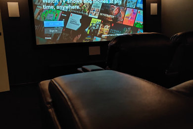 Photo of a mid-sized modern enclosed home theatre in Melbourne with black walls, carpet, a projector screen and black floor.