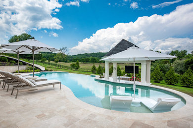 Classic back custom shaped infinity swimming pool in DC Metro with a water slide and natural stone paving.