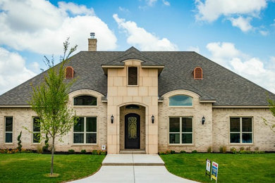 Large country beige two-story brick house exterior photo in Dallas with a hip roof and a shingle roof