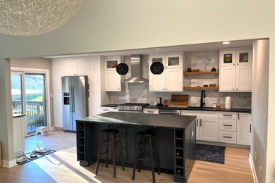 Eat-in kitchen - mid-sized modern single-wall light wood floor eat-in kitchen idea in New York with an undermount sink, shaker cabinets, white cabinets, granite countertops, gray backsplash, marble backsplash, stainless steel appliances, an island and black countertops