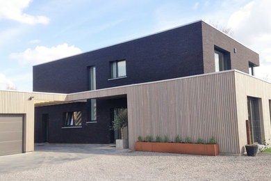 Exemple d'une grande façade de maison noire tendance en brique à un étage avec un toit plat.