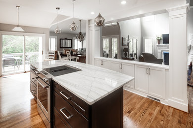 This is an example of a mid-sized traditional l-shaped eat-in kitchen in Charlotte with a farmhouse sink, shaker cabinets, white cabinets, quartzite benchtops, grey splashback, ceramic splashback, stainless steel appliances, light hardwood floors and with island.
