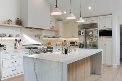 Large danish l-shaped light wood floor, beige floor and vaulted ceiling eat-in kitchen photo in Los Angeles with a farmhouse sink, beaded inset cabinets, white cabinets, quartzite countertops, white backsplash, stone slab backsplash, stainless steel appliances, an island and white countertops