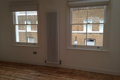 Medium sized contemporary master bedroom in London with white walls, light hardwood flooring and a standard fireplace.