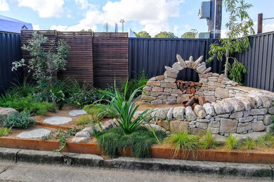 This is an example of a small and australian native beach style full sun xeriscape in Sunshine Coast with a retaining wall and natural stone pavers.