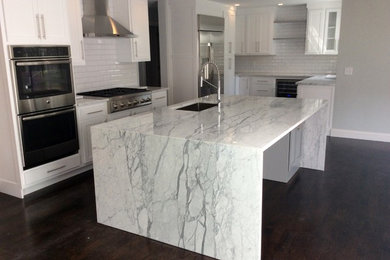 Example of a large transitional galley dark wood floor and brown floor eat-in kitchen design in Boston with an undermount sink, shaker cabinets, white cabinets, marble countertops, white backsplash, ceramic backsplash, stainless steel appliances and an island