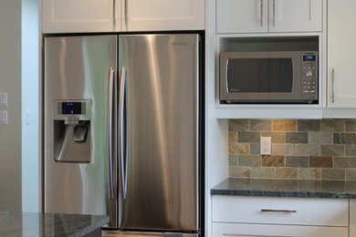 Open concept kitchen - mid-sized traditional u-shaped medium tone wood floor open concept kitchen idea in Vancouver with an undermount sink, shaker cabinets, white cabinets, granite countertops, multicolored backsplash, stone tile backsplash, stainless steel appliances and an island