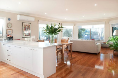 This is an example of a mid-sized modern u-shaped kitchen in Melbourne with a double-bowl sink, flat-panel cabinets, white cabinets, quartz benchtops, white splashback, ceramic splashback, with island, brown floor, white benchtop and medium hardwood floors.