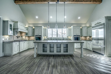 Example of a large tuscan u-shaped dark wood floor and brown floor kitchen design in Austin with a farmhouse sink, stone tile backsplash, stainless steel appliances, multicolored backsplash, an island, raised-panel cabinets and white cabinets