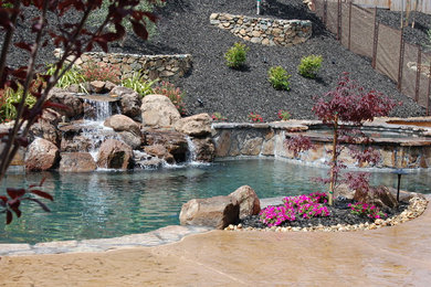 Photo of a large tropical backyard custom-shaped pool in Sacramento with a water feature and stamped concrete.