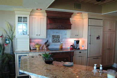 Mid-sized beach style u-shaped dark wood floor and brown floor eat-in kitchen photo in Other with a farmhouse sink, louvered cabinets, yellow cabinets, granite countertops, beige backsplash, stone tile backsplash, paneled appliances, a peninsula and multicolored countertops
