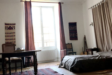 Réalisation d'une très grande chambre parentale tradition avec un mur blanc, tomettes au sol, une cheminée standard et un manteau de cheminée en pierre.