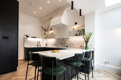 Foto på ett mellanstort funkis vit kök, med en enkel diskho, släta luckor, svarta skåp, bänkskiva i kvarts, vitt stänkskydd, integrerade vitvaror, laminatgolv, en halv köksö och brunt golv